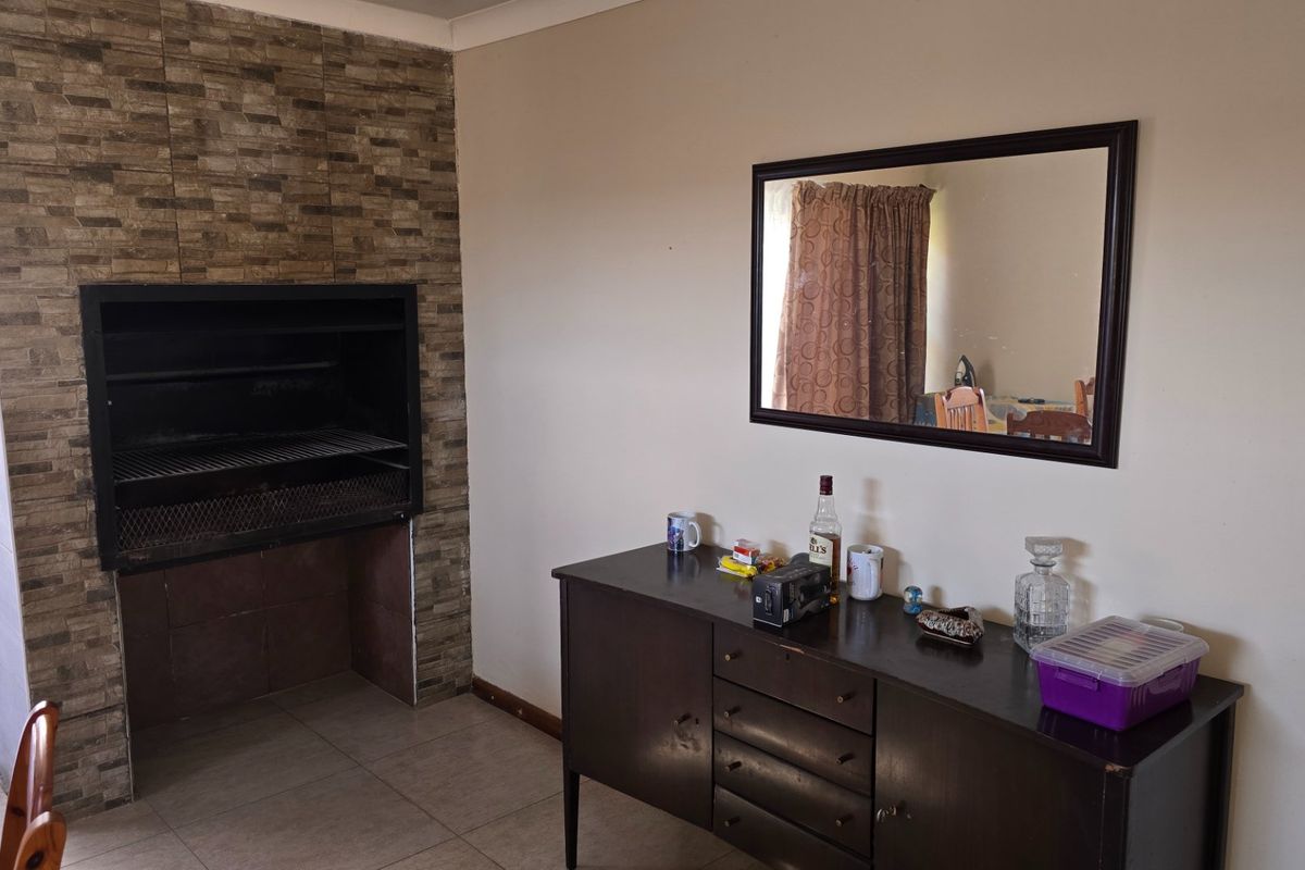 Indoor entertainment area featuring a built-in brick-clad braai fireplace and tiled flooring, providing a functional space for social gatherings.