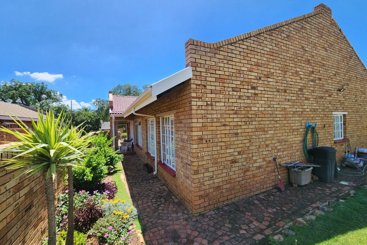 A side view of the townhouse featuring classic face brick construction, paved pathways, and established garden landscaping.