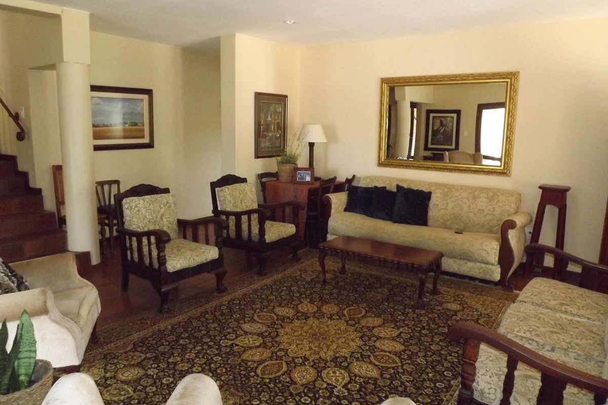 A spacious living room featuring recessed downlighting, a wooden staircase, and a structural column, offering a traditional layout with neutral wall finishes.