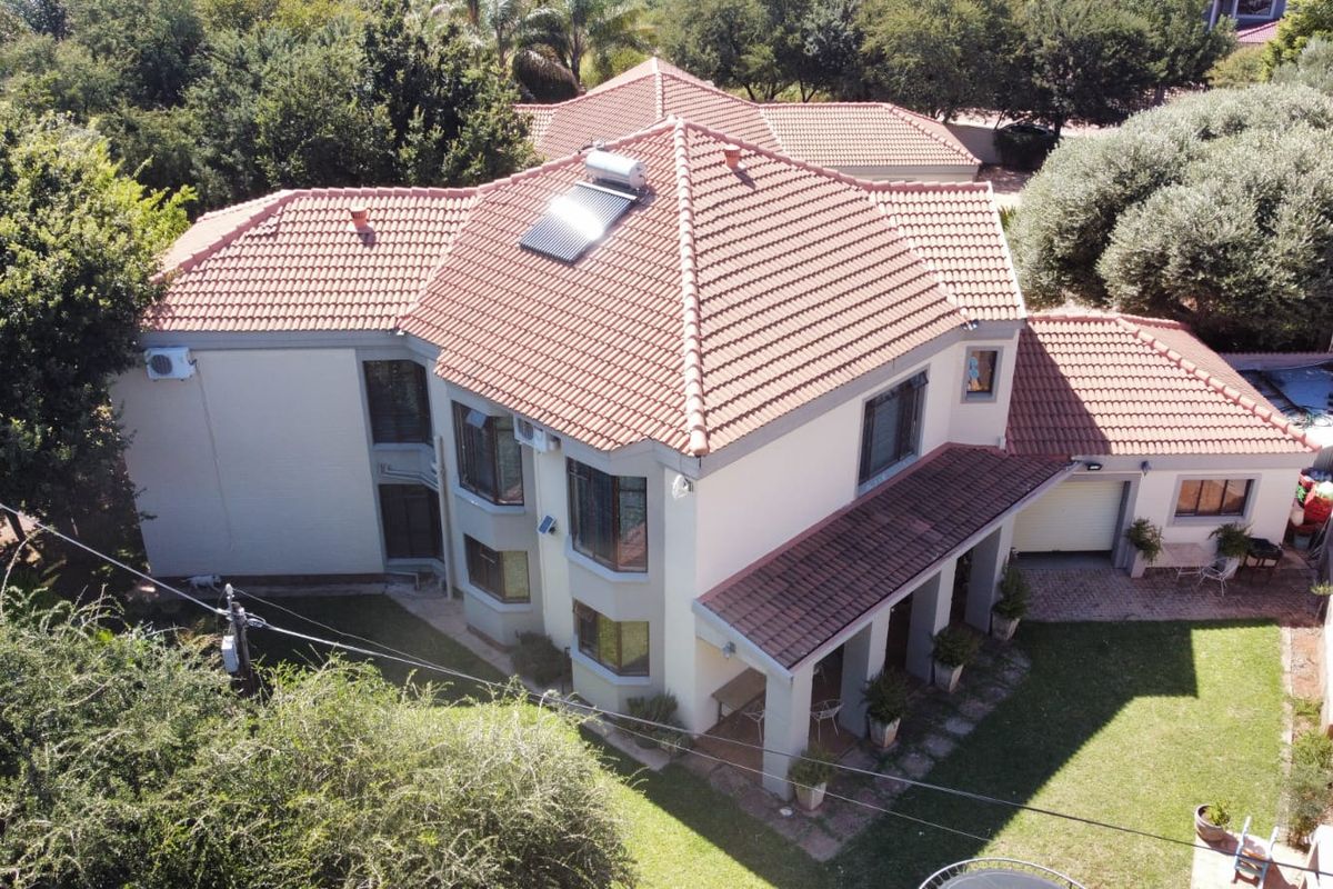 Aerial view of a double-story residential property featuring a terracotta tile roof, solar water heating, covered patio, and established garden surroundings.