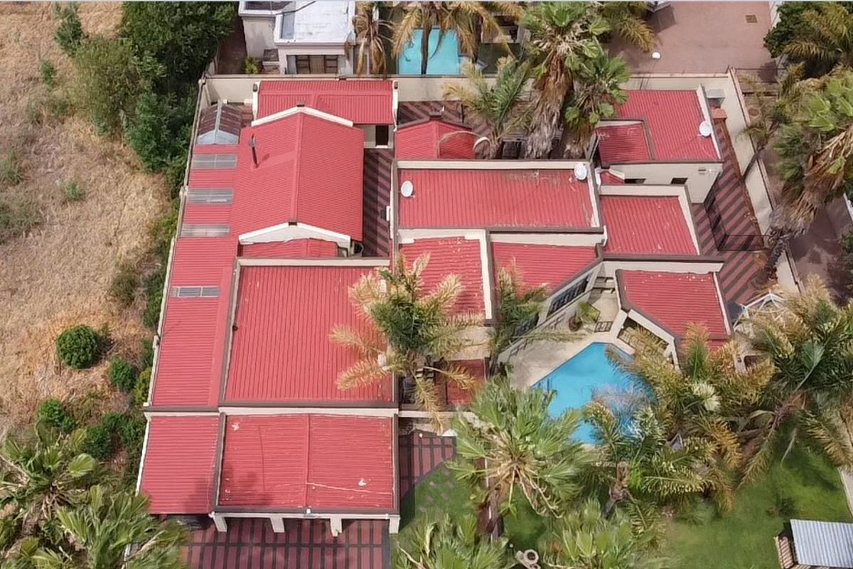 Aerial view of the property showcasing the red metal roof, swimming pool, and surrounding garden area.