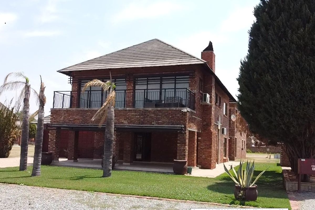 A two-story brick house featuring a covered ground-floor patio, an upper-level balcony with metal railings, and a chimney.