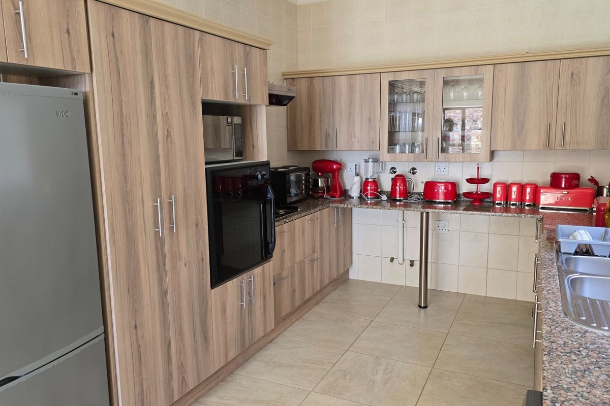 A functional kitchen featuring wood-look cabinetry, granite countertops, built-in oven, extractor fan, and a double bowl sink with tiled finishes.