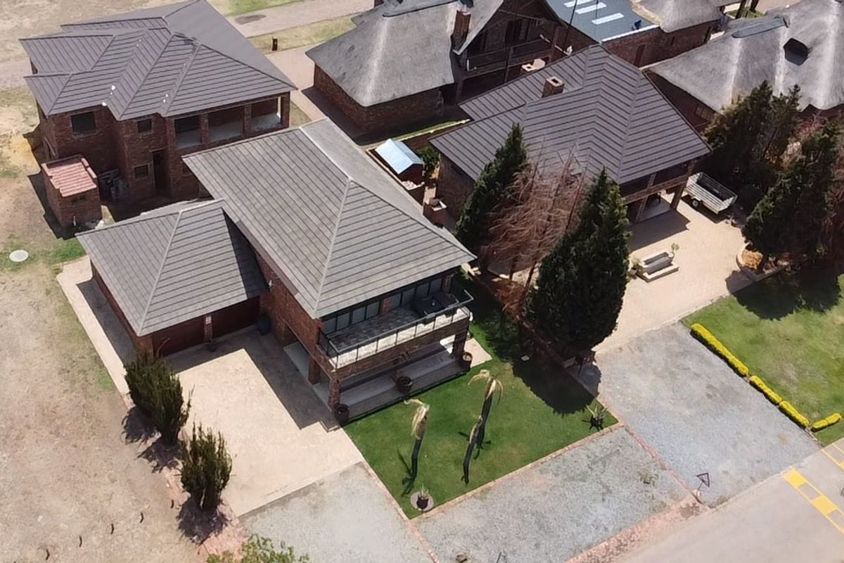 Aerial view of a residential property featuring a brick exterior, tiled roof, balcony, and a well-maintained garden with a paved driveway.