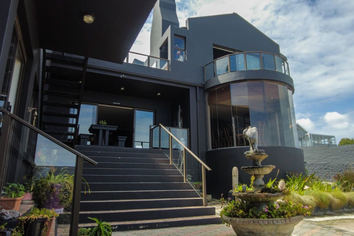 Rear exterior view of a modern multi-level home featuring a curved glass facade, balcony, and external staircase leading to the main living area.