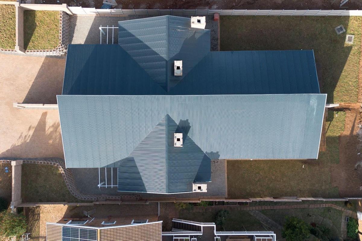 Aerial view of the property showing the corrugated metal roof, chimneys, surrounding lawn, and paved driveway area.
