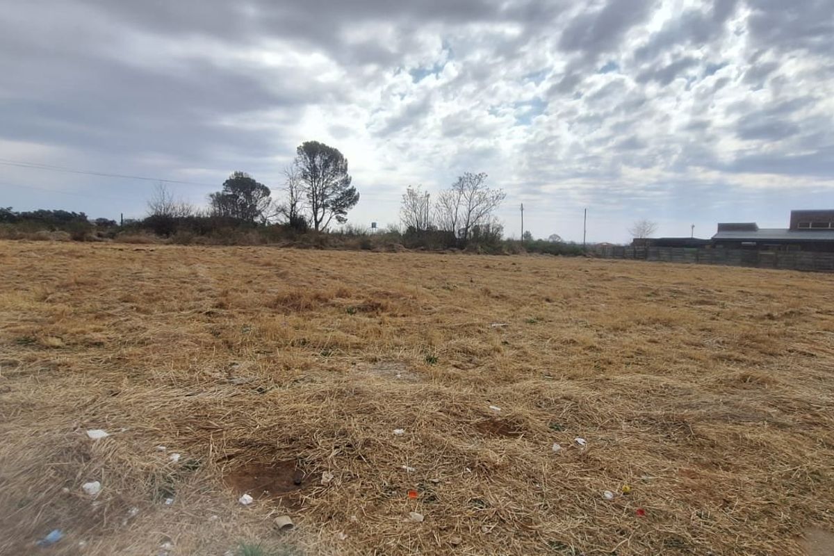 A vacant residential plot of land featuring dry grass, a utility pole, and perimeter fencing, offering a clear space for future development.