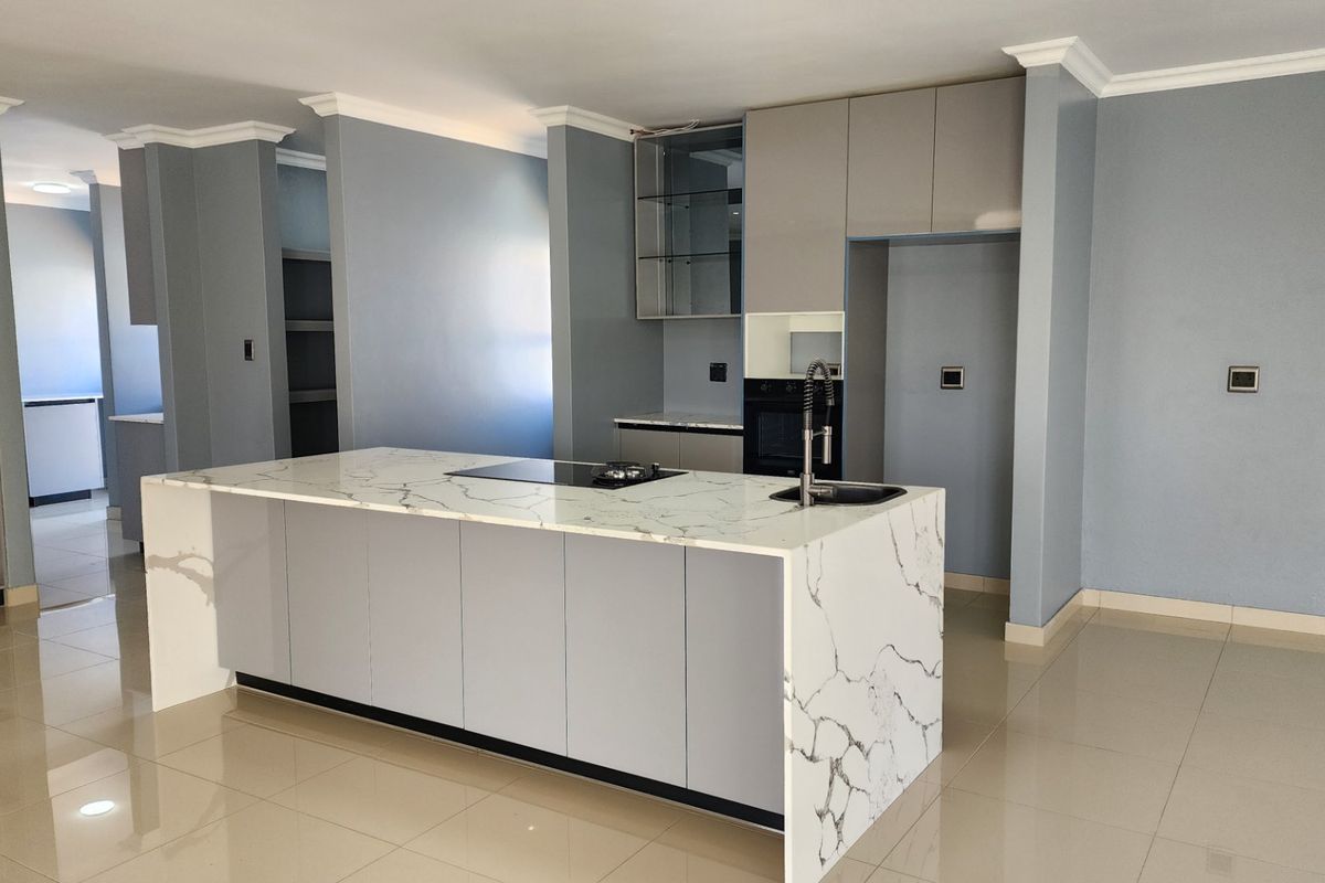 Modern kitchen featuring a large marble-look stone island, built-in oven, sleek cabinetry, and tiled flooring in an open-plan layout.