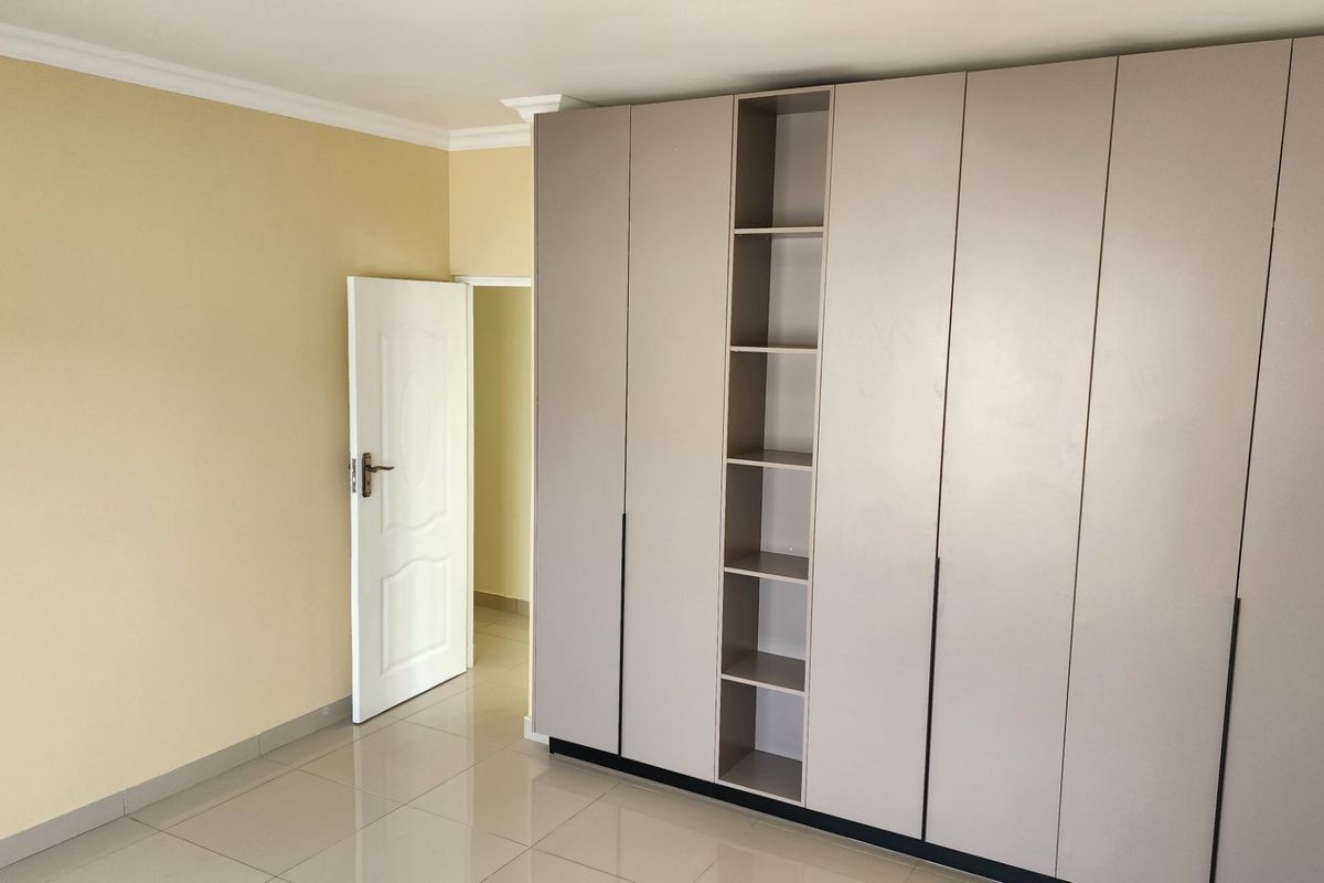 A clean, empty bedroom featuring modern built-in cupboards with integrated shelving and neutral tiled flooring.