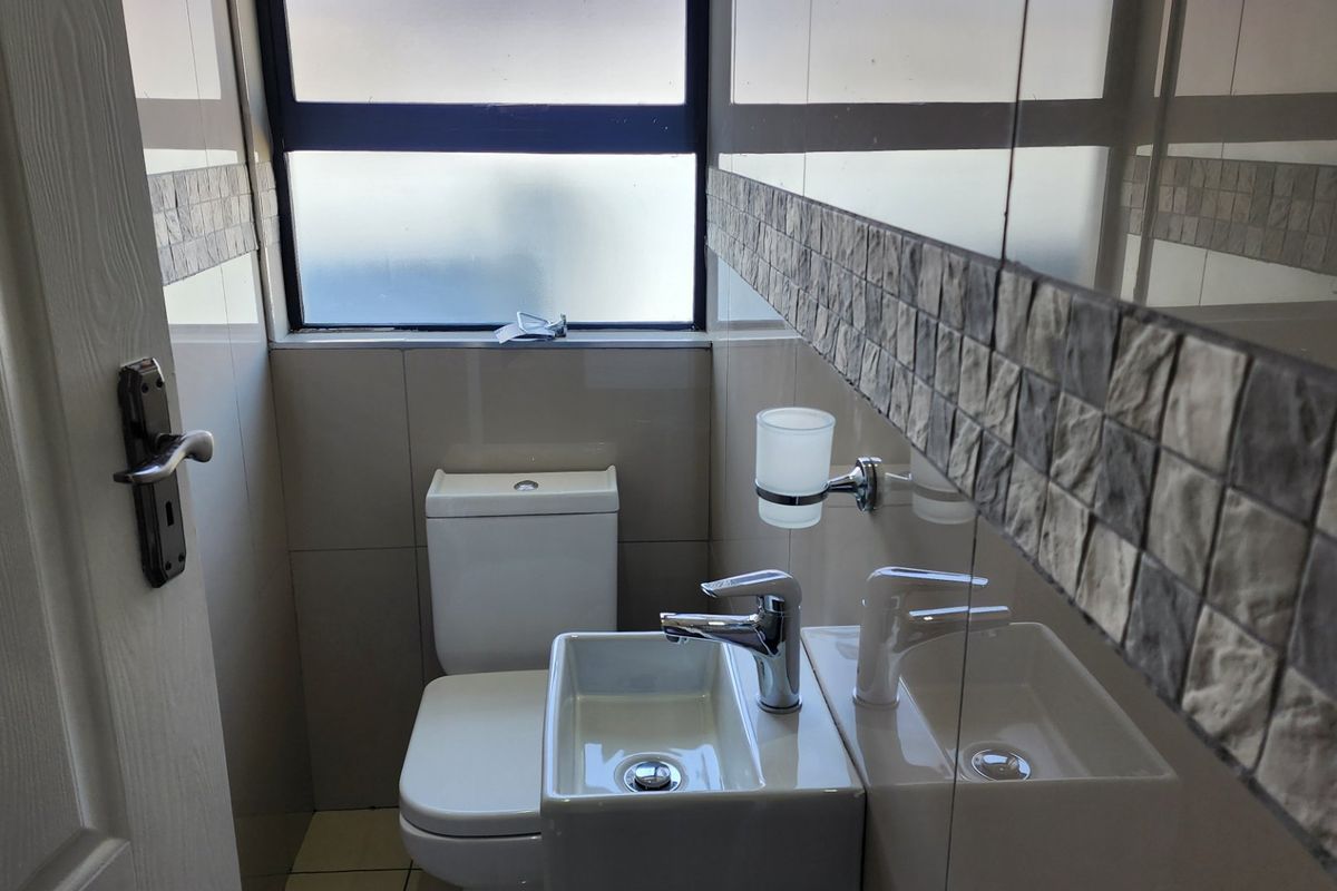 A compact, modern guest bathroom featuring a wall-mounted basin, toilet, and tiled finishes with a large wall mirror.
