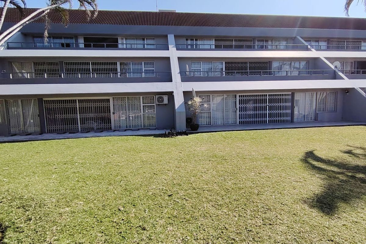 Rear view of a multi-story apartment complex featuring private balconies with security gates and a well-maintained communal lawn area.