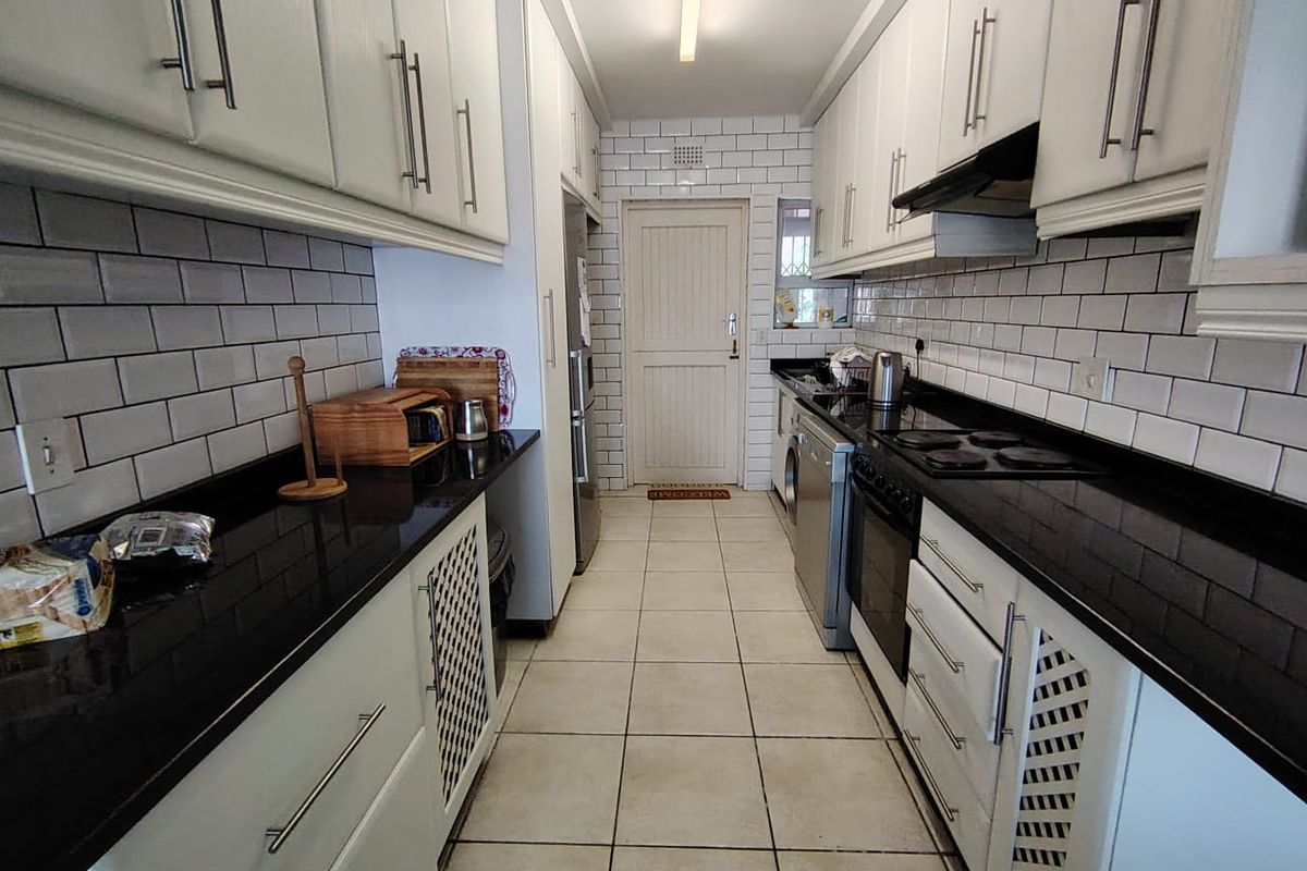 A galley-style kitchen featuring white cabinetry, black countertops, subway tile backsplash, and tiled flooring with a rear access door.