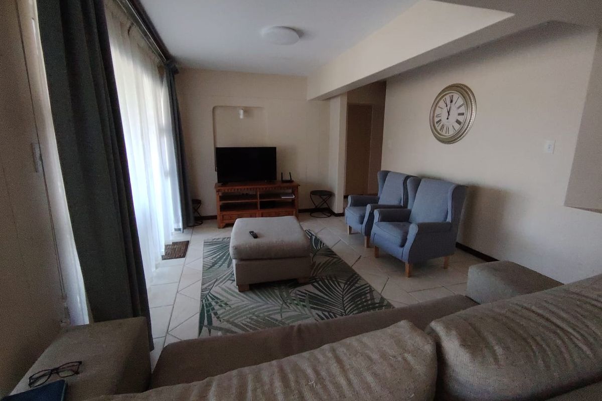 A comfortable living room featuring tiled flooring, recessed ceiling detail, and large windows allowing for natural light.
