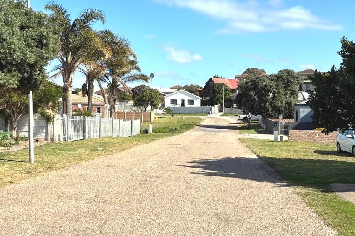A view of a residential street featuring a gravel road, perimeter fencing, and established palm trees in a suburban neighborhood setting.