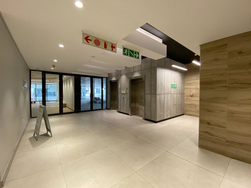 Modern commercial building lobby featuring elevator access, contemporary tiled flooring, and high-quality finishes with clear directional and fire safety signage.