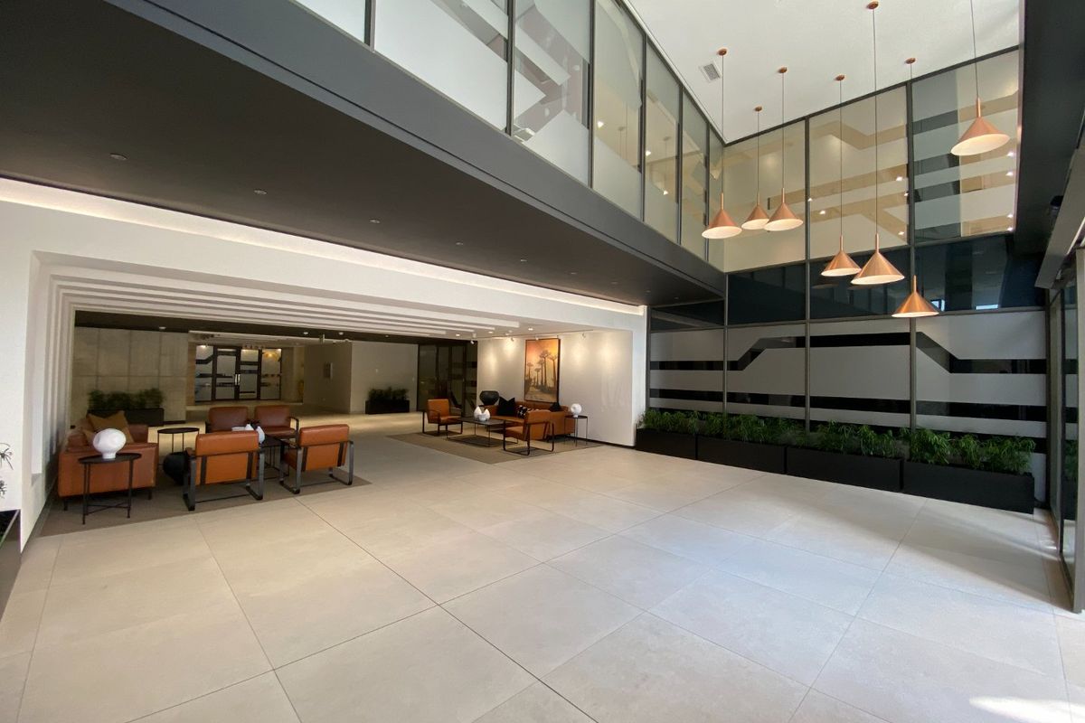 Spacious commercial entrance lobby featuring double volume ceilings, large format floor tiles, modern glass partitions, and elegant pendant lighting.