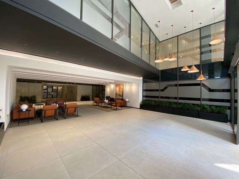 Spacious commercial entrance lobby featuring double volume ceilings, large format floor tiles, modern glass partitions, and elegant pendant lighting.