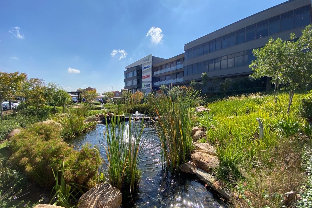 A well-maintained commercial office building exterior featuring a landscaped garden with a decorative pond and water feature in the foreground.