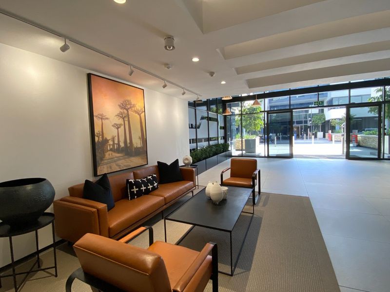 Modern commercial building entrance lobby featuring large glass facade, tiled flooring, and professional recessed and track lighting.