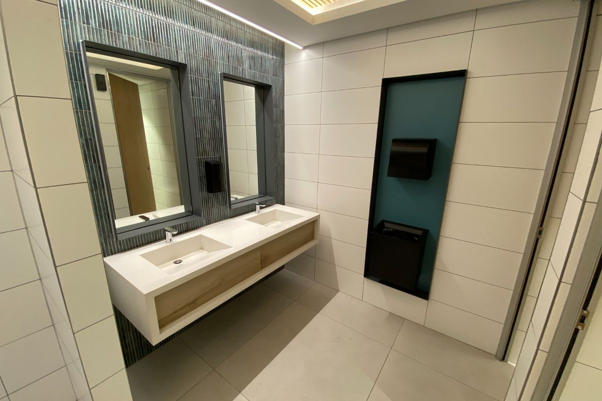 Modern commercial bathroom featuring a sleek double vanity with integrated sinks, contemporary tiled walls, and recessed architectural lighting.