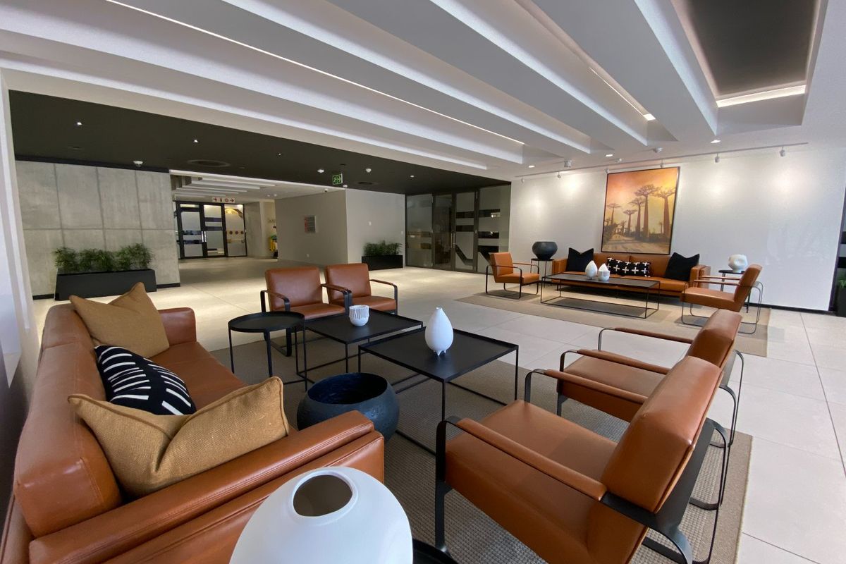 A spacious and modern commercial lobby or lounge area featuring a coffered ceiling, tiled floors, and a contemporary concrete feature wall.