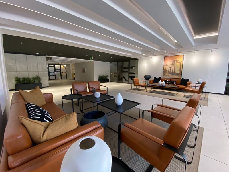 A spacious and modern commercial lobby or lounge area featuring a coffered ceiling, tiled floors, and a contemporary concrete feature wall.