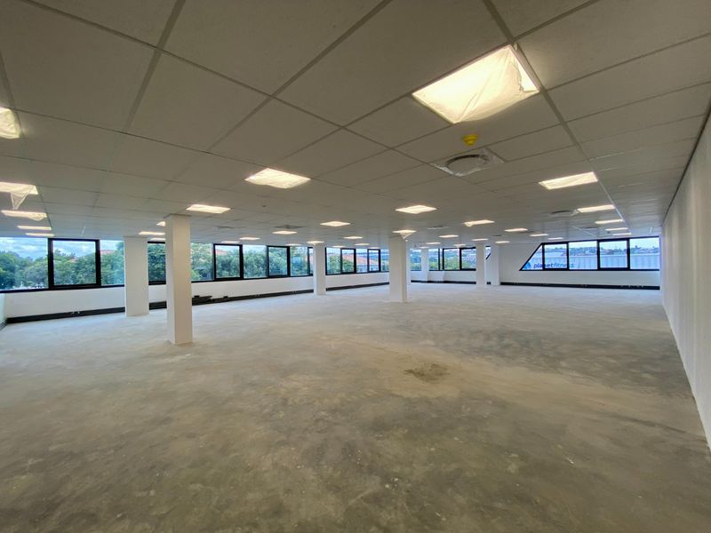 A large, open-plan commercial office space featuring a suspended ceiling, recessed lighting, and expansive windows providing natural light and views.