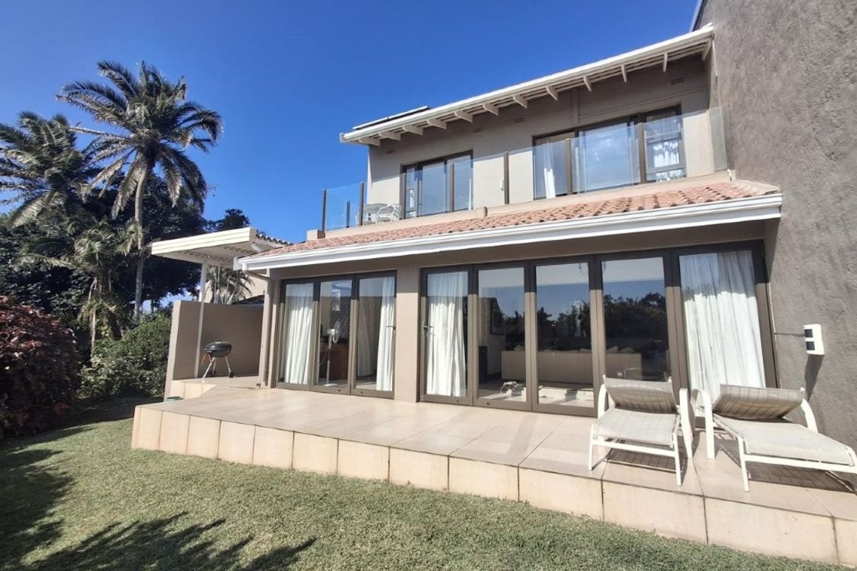 Rear view of the townhouse featuring a spacious tiled patio, large glass sliding doors, and an upper-level balcony with a modern glass balustrade.