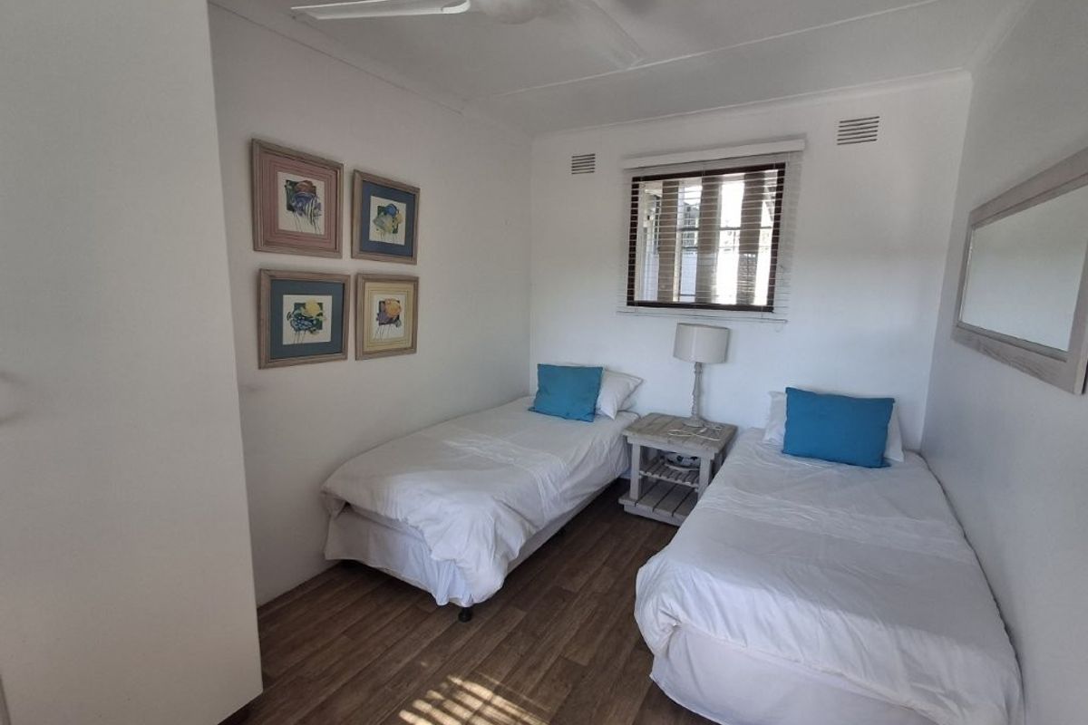 A compact bedroom featuring laminate flooring, a ceiling fan, and a window with fitted blinds.