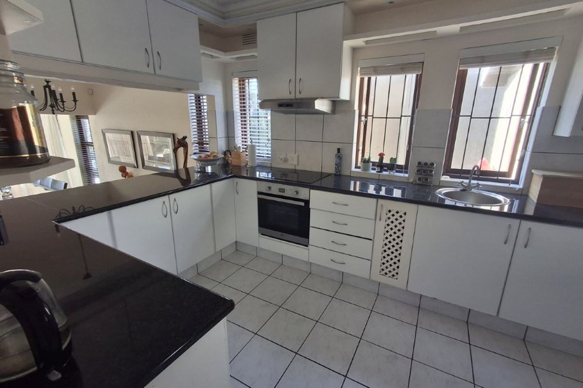 A functional U-shaped kitchen featuring white cabinetry, dark granite countertops, built-in oven and hob, and tiled flooring with natural light.