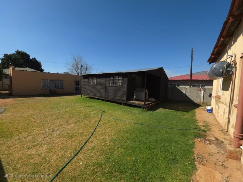 Spacious rear garden featuring a detached timber cabin, lawn area, and concrete boundary walling.