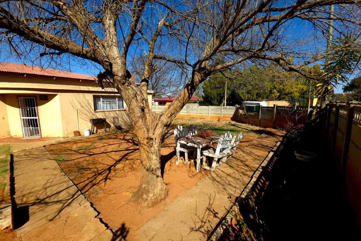 Rear exterior view of the property featuring a paved courtyard, mature tree, and precast concrete boundary walling.
