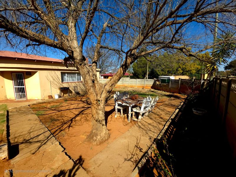Rear exterior view of the property featuring a paved courtyard, mature tree, and precast concrete boundary walling.