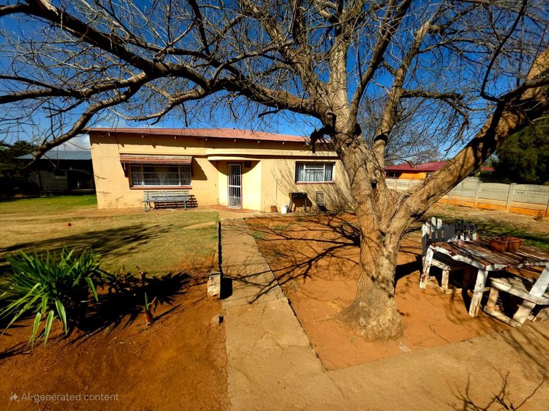Rear view of a single-story house featuring a corrugated metal roof, concrete pathway, and a large mature tree in the garden area.