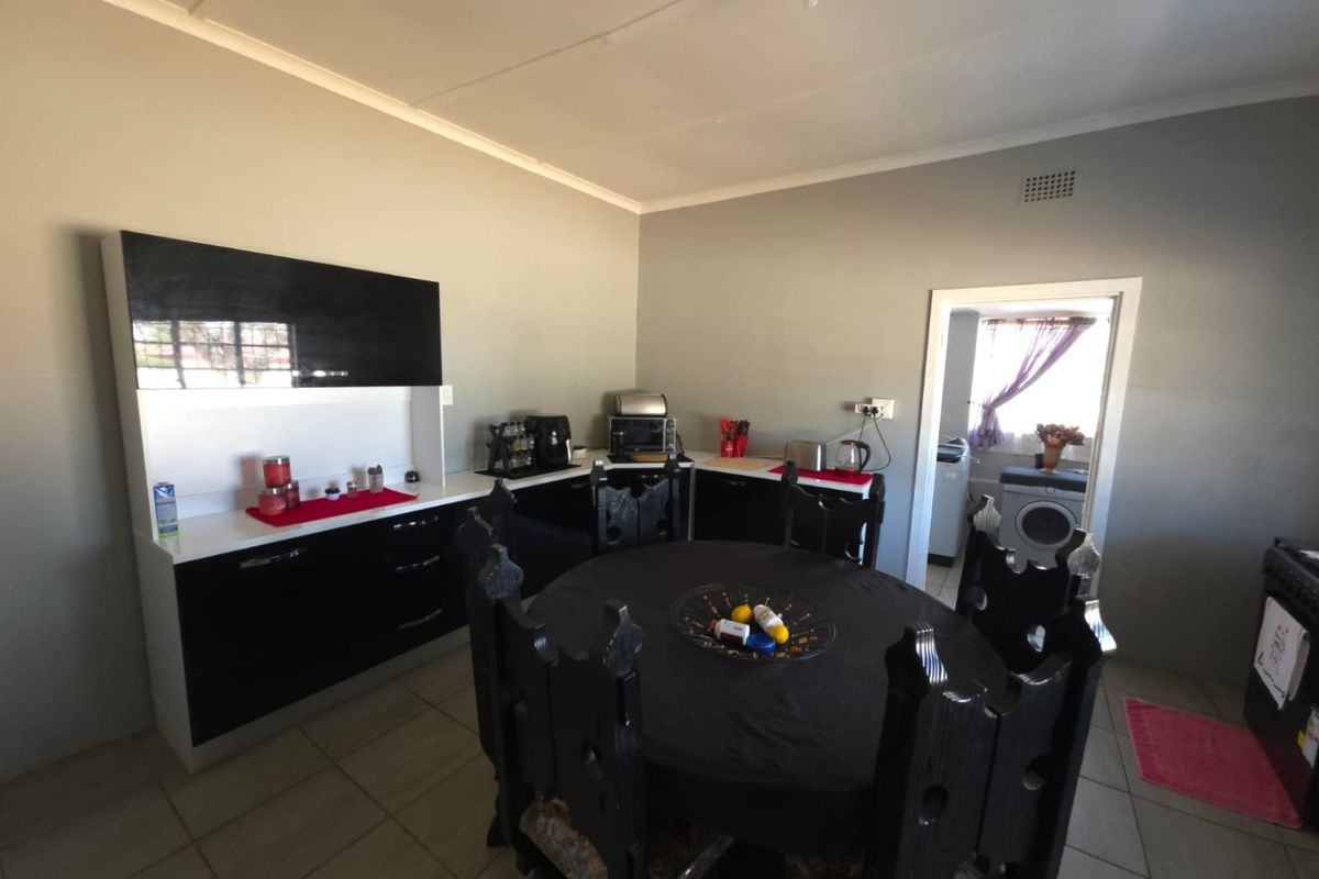 A functional kitchen featuring modern black cabinetry, contrasting countertops, and tiled flooring, with an adjacent scullery area visible through the doorway.