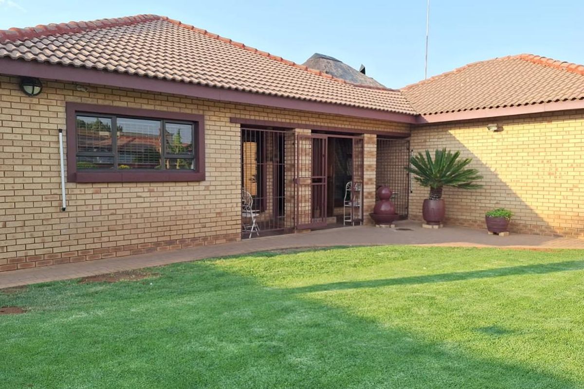 Rear view of the townhouse featuring a face brick facade, tiled roof, paved walkway, and a well-maintained lawn area.
