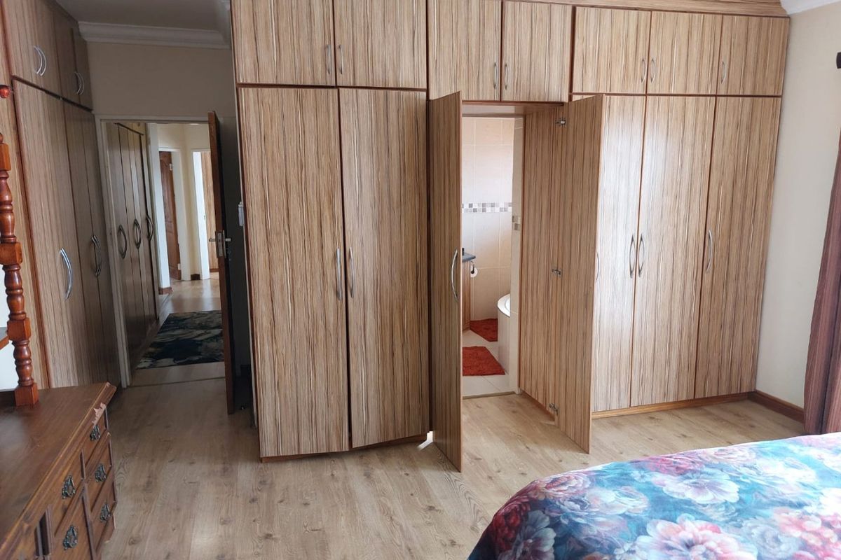 Bedroom featuring extensive floor-to-ceiling built-in wooden cupboards, laminate flooring, and direct access to an en-suite bathroom.
