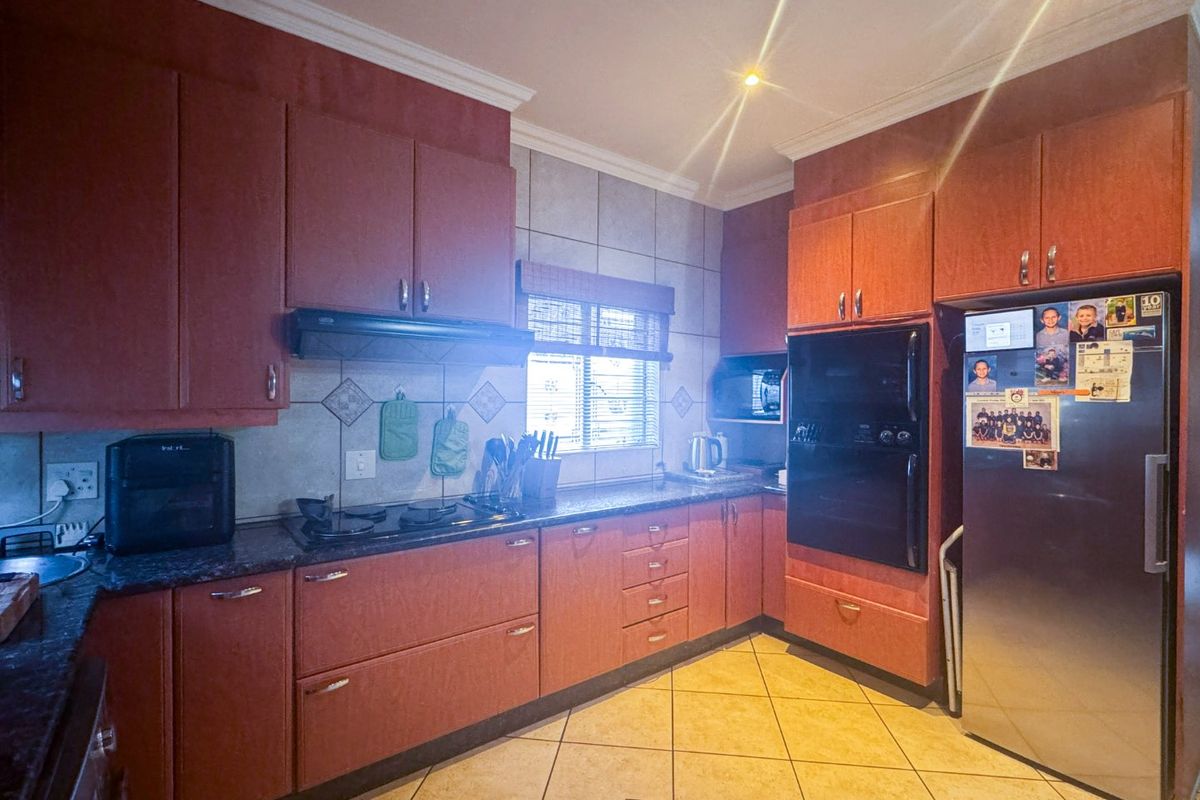 A functional kitchen featuring dark wood-finish cabinetry, granite countertops, a built-in oven, and a ceramic hob with an extractor fan.