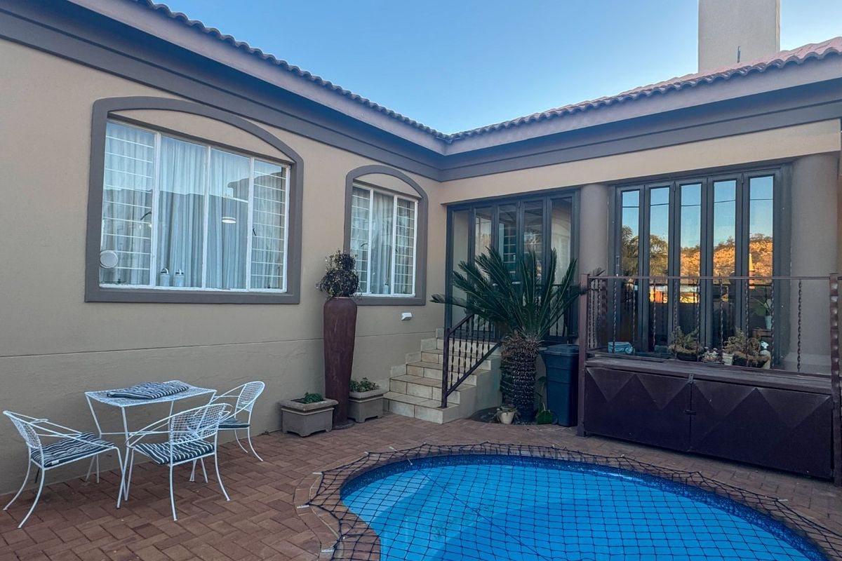 A private rear courtyard featuring a swimming pool with safety net, paved patio area, and direct access to the home via glass sliding doors.