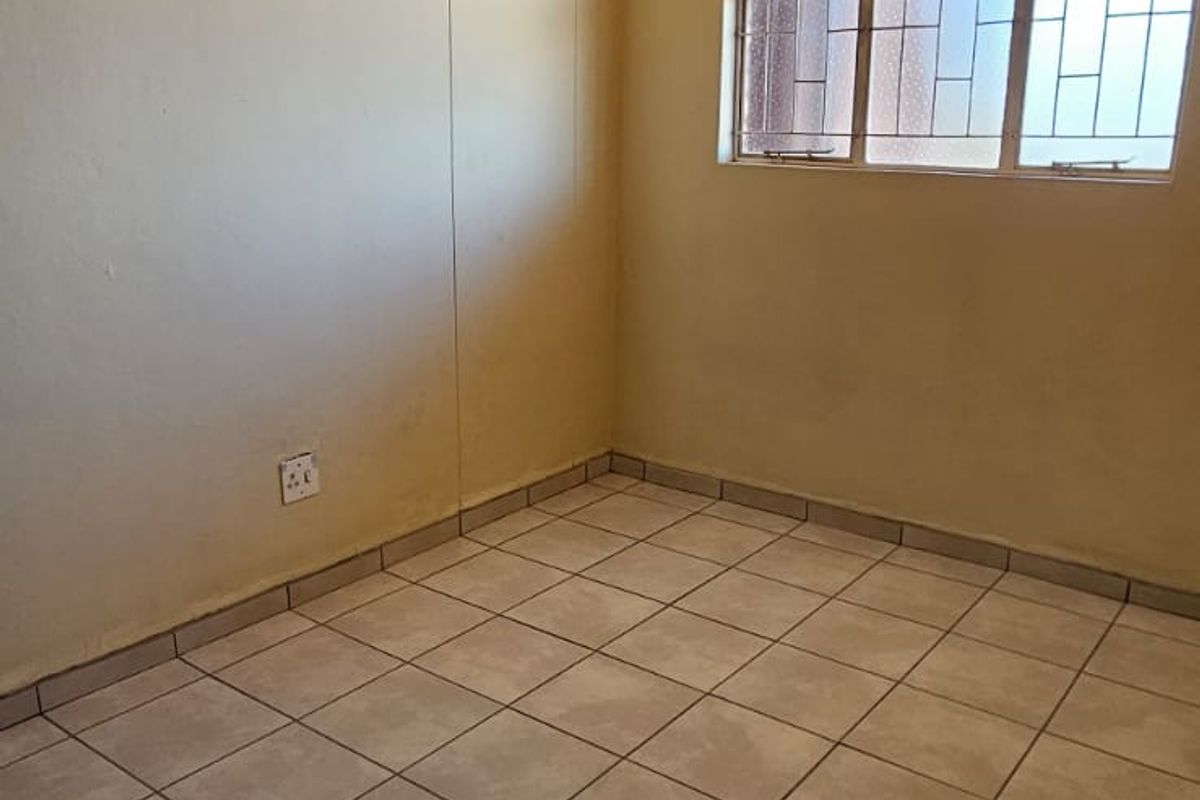 An empty bedroom featuring tiled flooring, a textured ceiling, and a window fitted with security bars.
