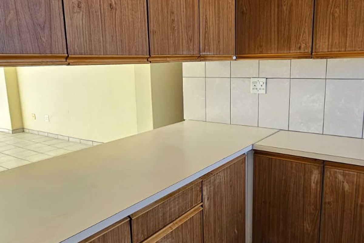 A dated kitchen featuring wood-look laminate cabinetry, tiled backsplash, and ceramic floor tiles, offering a blank canvas for modern renovation.