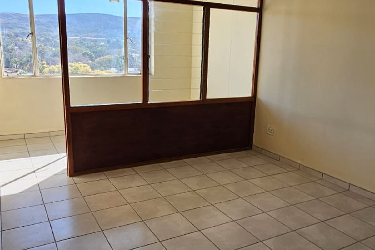 An empty living area featuring tiled flooring, a textured ceiling, and a timber-framed glass partition offering natural light and scenic views.