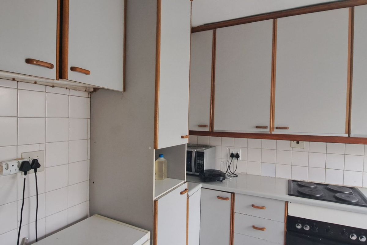 A functional kitchen featuring dated cabinetry, tiled backsplash, and integrated electric cooking appliances, offering potential for a modern renovation.