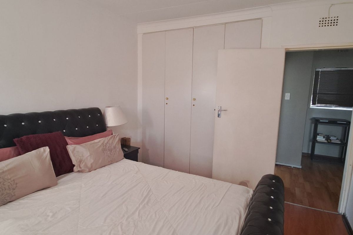 A bedroom featuring built-in cupboards, laminate flooring, and a ventilation grille, with an adjacent room visible through the doorway.