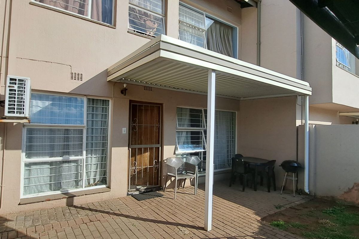 Rear exterior view of the apartment featuring a paved patio area with a covered roof, security gates, and window bars.