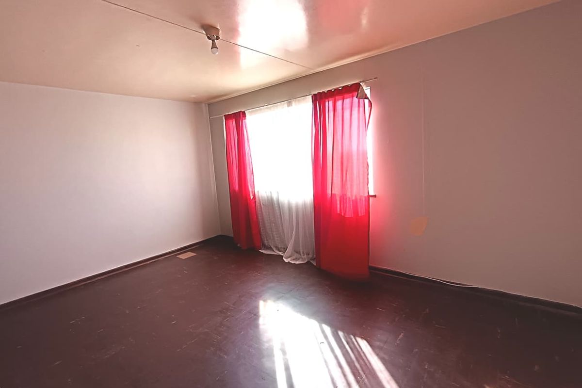 An empty bedroom featuring dark hardwood flooring and a large window, providing a blank canvas for renovation or interior design updates.