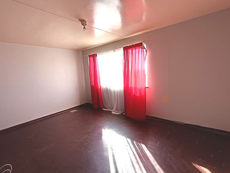 An empty bedroom featuring dark hardwood flooring and a large window, providing a blank canvas for renovation or interior design updates.