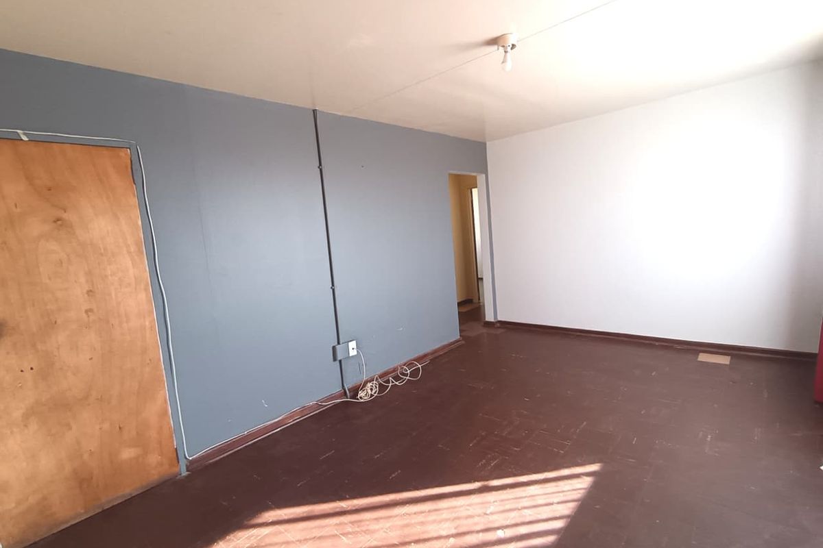 An empty living room featuring dark vinyl flooring, two-tone painted walls, and exposed surface-mounted electrical conduit.