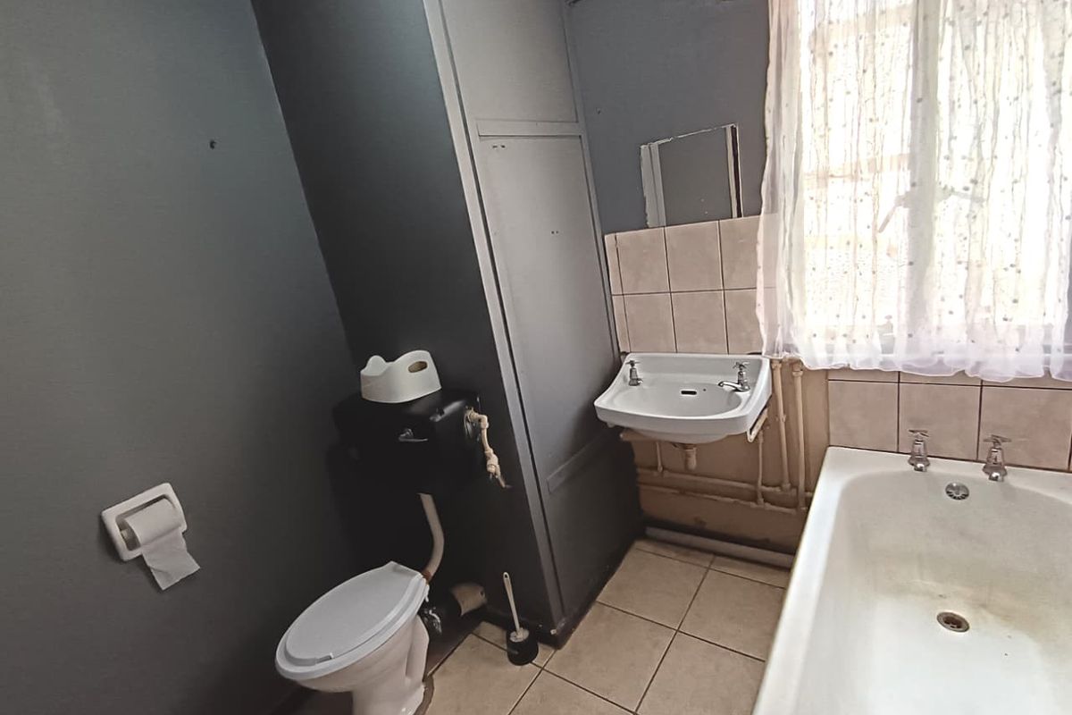 A dated bathroom featuring a standard bathtub, wall-mounted basin, and low-level toilet, with tiled flooring and splashbacks, offering potential for modernization.