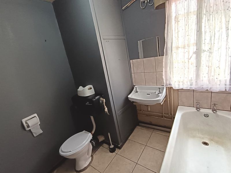 A dated bathroom featuring a standard bathtub, wall-mounted basin, and low-level toilet, with tiled flooring and splashbacks, offering potential for modernization.